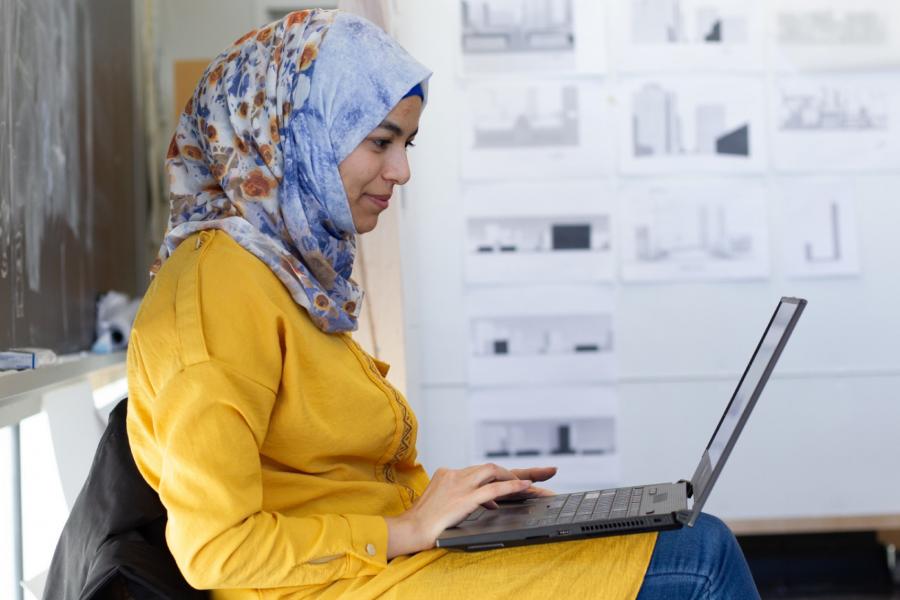 A woman dressed in yellow types on a laptop while seated. 